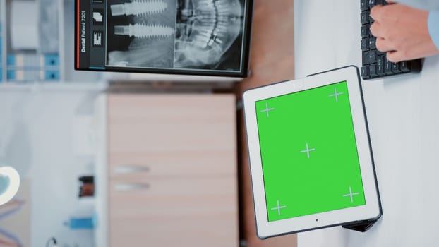 Vertical video: Close up of horizontal green screen on digital tablet at dentist office. Stomatologist using mockup template and isolated background on gadget for dentistry and oral care
