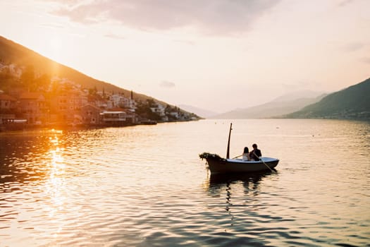 Man and woman are sailing in a boat with oars on the sea against the sunset sky. High quality photo