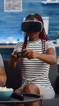 Married interracial couple using technology at home. African american woman with vr glasses playing game while caucasian man watching and cheering in living room. Mixed race cheerful people