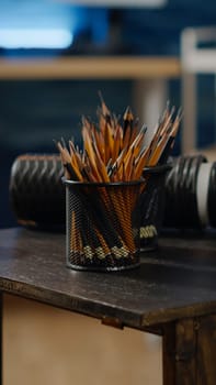 Close up of wooden table with colorful pencils for artist in studio space. Empty creativity room with nobody but artistic equipment, tools, white vase. Professional workshop for craft industry