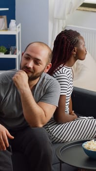 Interracial couple with dispute and marriage problems yelling on couch in living room. Multi ethnic husband and wife having argument fighting at home. Angry partners in fight