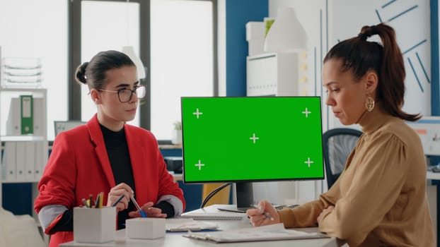 Women doing teamwork with isolated green screen on computer in business office. Workmates using copy space mock up template and background on chroma key display for startup work.