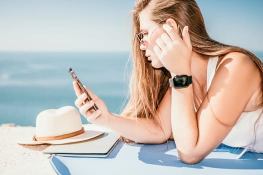 Successful business woman in yellow hat working on laptop by the sea. Pretty lady typing on computer at summer day outdoors. Freelance, travel and holidays concept.