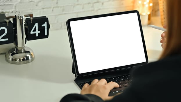 Over shoulder view of young woman using digital tablet on white working desk.