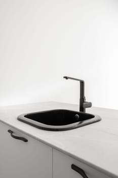 Stylish black kitchen sink in a white table on the white walls of the kitchen. Concept of high-tech modern plumbing and kitchen design. Comfort and design.