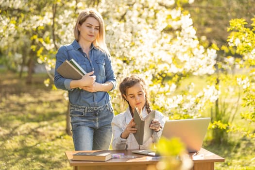 Woman and little girl laying on the spring flower field outdoors - having fun using a laptop