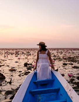 Asian women with a hat and dress in a boat at the Beautiful Red Lotus Sea Kumphawapi is full of pink flowers in Udon Thani in northern Thailand. Flora of Southeast Asia.