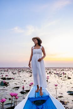 Asian women with a hat and dress in a boat at the Beautiful Red Lotus Sea Kumphawapi is full of pink flowers in Udon Thani in northern Thailand. Flora of Southeast Asia.