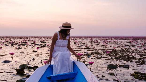 Asian women with a hat and dress in a boat at the Beautiful Red Lotus Sea Kumphawapi is full of pink flowers in Udon Thani in northern Thailand. Flora of Southeast Asia.