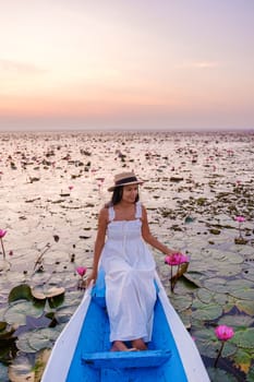 Asian women in a boat at the Beautiful Red Lotus Sea Kumphawapi is full of pink flowers in Udon Thani in northern Thailand. Flora of Southeast Asia.