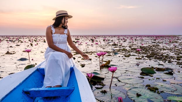 Asian women with a hat and dress in a boat at the Beautiful Red Lotus Sea Kumphawapi is full of pink flowers in Udon Thani in northern Thailand. Flora of Southeast Asia.