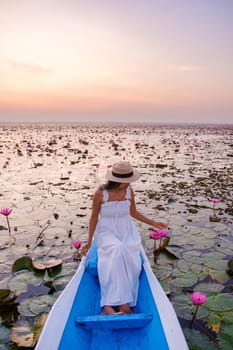 Asian women with a hat and dress in a boat at the Beautiful Red Lotus Sea Kumphawapi is full of pink flowers in Udon Thani in northern Thailand. Flora of Southeast Asia.