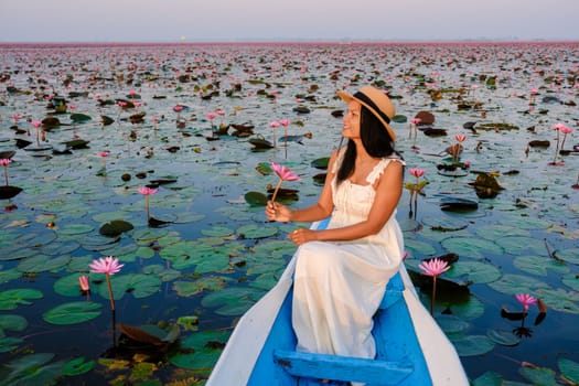 Asian women in a boat at the Beautiful Red Lotus Sea full of pink flowers in Udon Thani in northern Thailand. Flora of Southeast Asia.