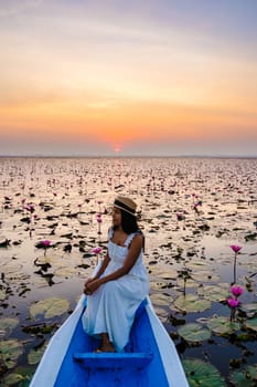 Asian women with a hat and dress in a boat at the Beautiful Red Lotus Sea Kumphawapi is full of pink flowers in Udon Thani in northern Thailand. Flora of Southeast Asia.