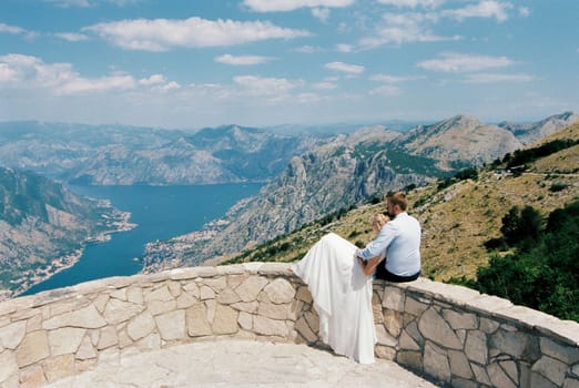 Bride and groom are sitting on an observation deck over the mountains. High quality photo