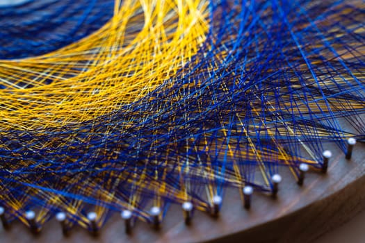 Colored thread mandala on a wooden board with nails. Mandala Moon Harmony Sun esotericism and psychology pictures from yellow and blue silk threads