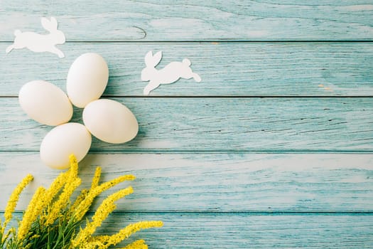 Happy Easter Day Concept. Flat lay of holiday banner background design white easter eggs and beautiful yellow flowers on blue wooden background with empty copy space, celebration greeting card