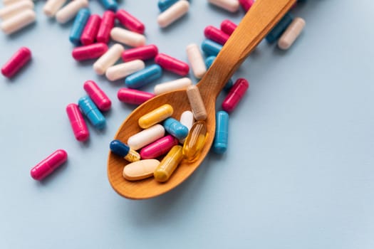 Various bright pills on a blue background lie in a wooden spoon against the background of different bright pills. Health care concept, close-up