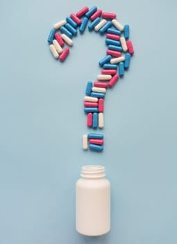 A question mark consisting of three multi-colored vitamins on a blue background along with a plastic white vial. Health problems and treatment. The concept of evidence-based medicine