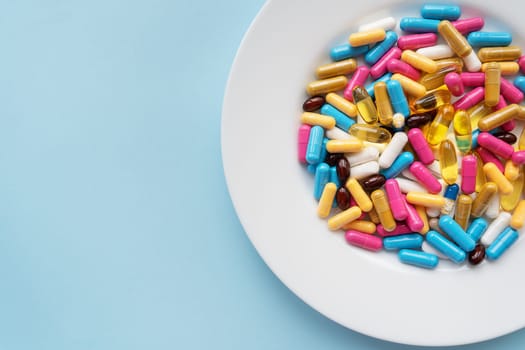 Colorful pills in a large white bowl on a blue background. The concept of health and evidence-based medicine