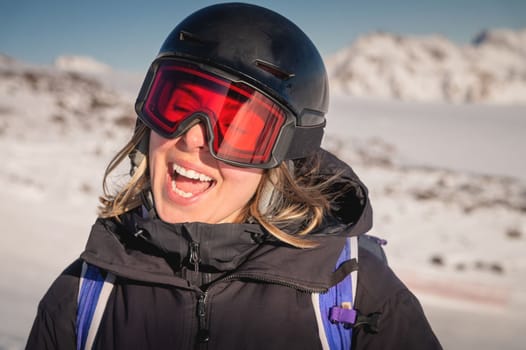 Portrait of a woman in the Alps. Smiling young woman in ski goggles and helmet stopped while skiing in ski resort.