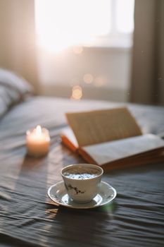 Light cozy bedroom, Coffee or tea cup and an open book on the bed. Spring still life. Breakfast in bed.