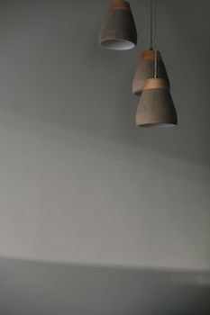 gray lamps with a wooden part is hanging by the gray wall background indoors.