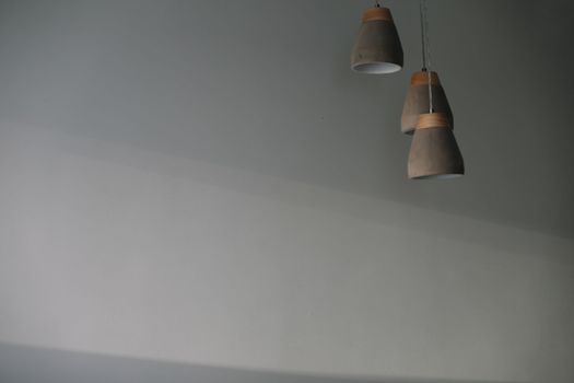 gray lamps with a wooden part is hanging by the gray wall background indoors.
