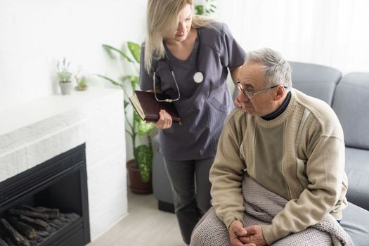 Caring nurse talks to old patient holds his hand sit in living room at homecare visit provide psychological support listen complains showing empathy encouraging. Geriatrics medicine caregiving concept.