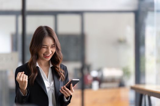 Young happy lucky Business woman feeling excited winner looking at cellphone using mobile phone winning online, receiving great news or sms offer.