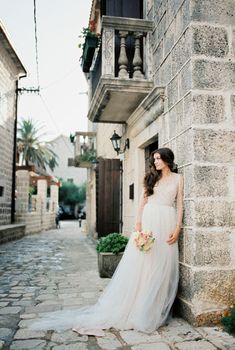 Bride in a white dress leaned against the stone facade of an old house. High quality photo