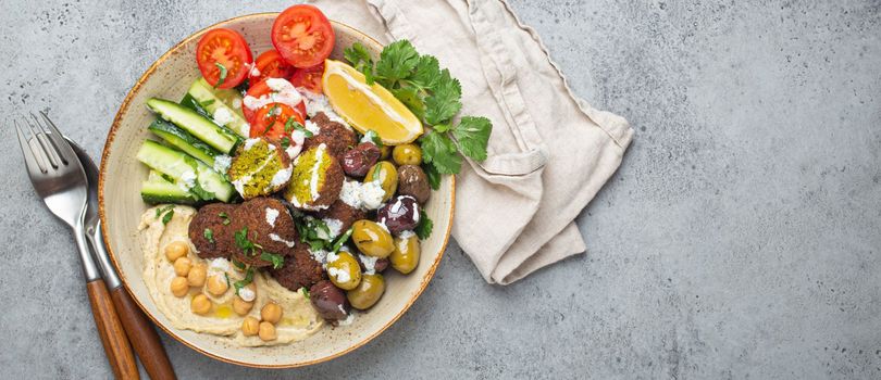 Falafel salad bowl with hummus, vegetables, olives, herbs and yogurt sauce. Vegan lunch plate top view on rustic stone background, healthy meal with falafel and veggies, space for text