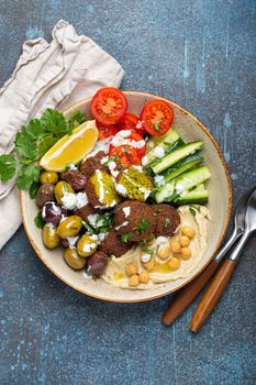 Falafel salad bowl with hummus, vegetables, olives, herbs and yogurt sauce. Vegan lunch plate top view on rustic stone background, healthy meal with falafel and veggies