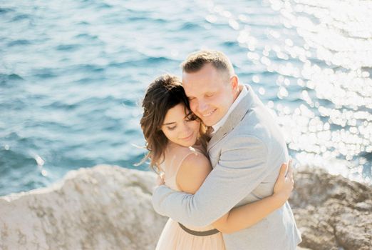 Groom hugs bride standing on a rock above the sea. High quality photo