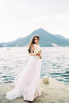 Bride with a bouquet stands on the pier against the backdrop of the mountains. High quality photo