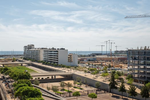 Gorg area in Barcelona, Spain, with many new and under construction residential buildings. Park areas with architectural bridges. In the distance, the ocean and blue sky merge into the horizon lines