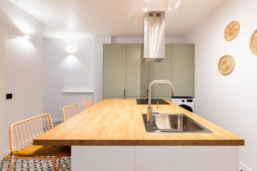 Designer kitchen with bright lighting from wall lamps. Table with sink and faucet in chromed metal. Above the electric stove, system for purifying the air from odors during cooking