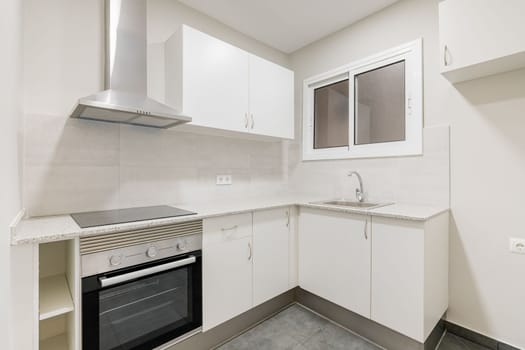 Light compact kitchen with stove, extractor hood and sink and window. Concept of kitchen in a small apartment. Modern minimalist design in new buildings.