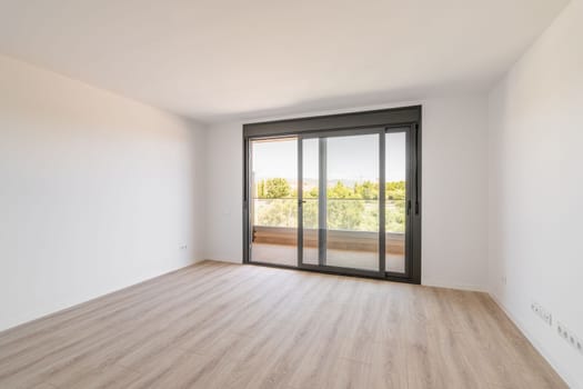 Spacious large room with wooden parquet structure and panoramic window overlooking beautiful landscape among complex of new buildings and balcony with elegant glass border. Mortgage and moving concept.