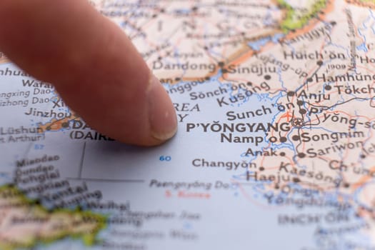 Finger pointing to Pyongyang, North Korea on colorful map with shallow depth of field, background blur. Concept geopolitical tensions. High quality photo
