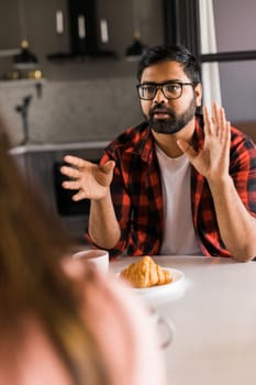 Happy couple eating breakfast and talking at dining table in morning. Indian girl and latin guy. Relationship and diversity