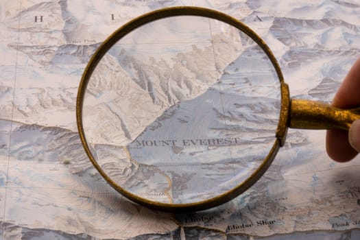 Hand holding magnifying glass showing map detail of Mt. Everest on a vintage topographical map. High quality photo