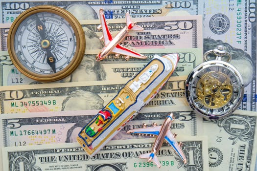 Miniature cruise ship, airplanes, compass and watch on top of US dollars 1 to 10, concept high cost of travel. High quality photo