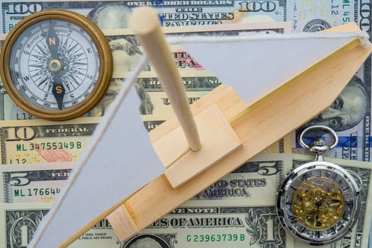 Layout of US currency cash with compass, clock, wooden boat on top, selective focus. High quality photo