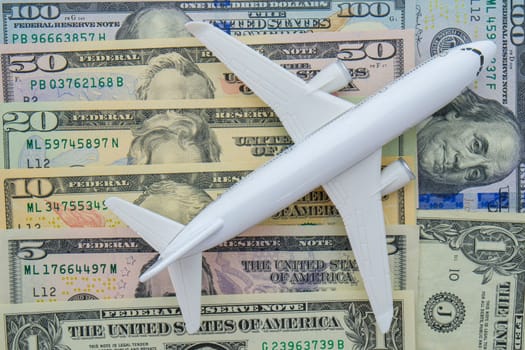 Passenger plane sitting on US currency bills of different denominations showing concept high cost of flying, travel. High quality photo