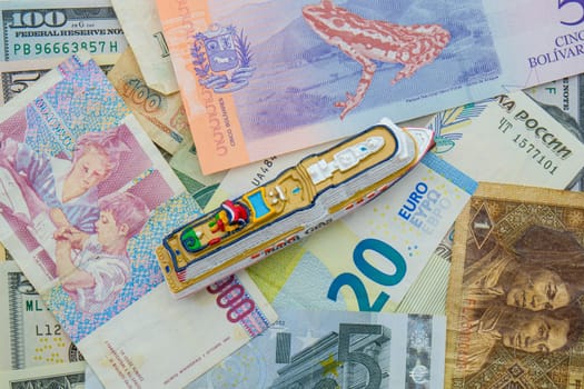 A miniature cruise ship on a background of international currencies including ruble, euro, USD top down view. High quality photo