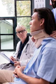 Nurse and medic helping asian patient with neck brace removing cervical neck collar after injury accident during appointment. Injured young adult healing fracture and trauma in hospital waiting area