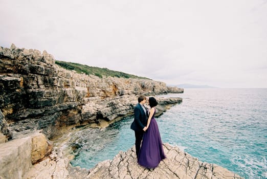 Man and woman stand hugging on a rock above the sea. High quality photo
