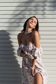 Young beautiful woman in a romantic dress with a floral print and a pearl necklace bracelet on the background of a light garage fence