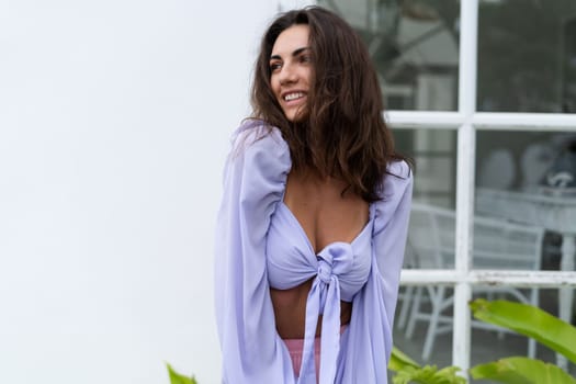 Pretty young stylish woman in trendy purple crop top long sleeve , pink skirt, isolated, white wall, tropical leaves natural day light..